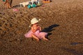 Smiling one-year-old girl in pink veil skirt and straw hat sits on the beach Royalty Free Stock Photo