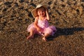 Smiling one-year-old girl in pink veil skirt and straw hat sits on the beach Royalty Free Stock Photo