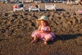 Smiling one-year-old girl in pink veil skirt and straw hat sits on the beach Royalty Free Stock Photo