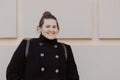 Smiling overweight brunette woman in a stylish black coat. Tourist student walking around with a backpack. Portrait of happy