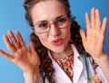 Smiling paediatrician woman playing peekaboo on blue