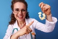 Smiling paediatrist woman pointing at garlic beads on blue