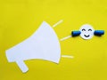 A smiling paper face with earplugs protects against the sounds of a loudspeaker. Noise protection, application on a