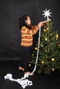 Smiling Papuan girl putting white paper chain on Christmas tree