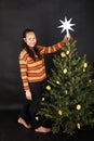 Smiling Papuan girl putting white star on top of Christmas tree