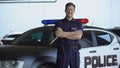 Smiling patrolman standing near car with crossed hands, carrying out duties