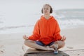 Smiling peaceful young woman in sportswear and headphones meditating with closed eyes while sitting in Lotus pose on Royalty Free Stock Photo