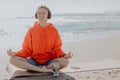 Smiling peaceful young woman in sportswear and headphones meditating with closed eyes while sitting in Lotus pose on Royalty Free Stock Photo