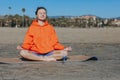 Smiling peaceful young woman in sportswear and headphones meditating with closed eyes while sitting in Lotus pose on Royalty Free Stock Photo