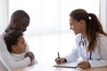 Smiling pediatrician doctor talking to African American child at meeting