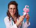 Smiling pediatrist woman listening toy with stethoscope on blue