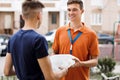 A smiling person wearing an orange T-shirt and a name tag is delivering a parcel to a client. Friendly worker, high