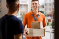 A smiling person wearing an orange T-shirt and a name tag is delivering parcels to a client. Friendly worker, high
