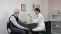 Smiling pharmacist holding a bottle of pills and pointing them to senior patient.