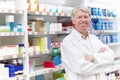 Smiling pharmacist near shelf at medical store. Portrait of mature pharmacist smiling with hands folded near shelf at Royalty Free Stock Photo