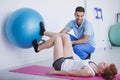 Physiotherapist supporting woman exercising with rehabilitation ball