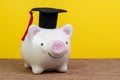 Smiling pink piggy bank wearing graduated hat on wooden table, yellow background and copy space, education fund, Scholarships, Royalty Free Stock Photo