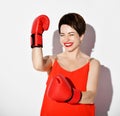 Happy laughing beautiful brunette woman with short hair in red dress, earrings and boxing gloves holds hand up