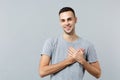 Smiling pleasant young man in casual clothes looking camera, holding palms crossed on heart chest isolated on grey Royalty Free Stock Photo