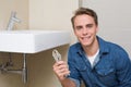 Smiling plumber with wrench by sink in bathroom Royalty Free Stock Photo