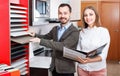 Smiling polite saleswoman helping man to choose materials for kitchen furniture in shop