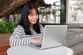 A smiling and positive Asian woman is working remotely outdoors in a city park, using her laptop Royalty Free Stock Photo