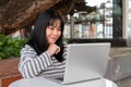 A smiling and positive Asian woman is working remotely outdoors in a city park, using her laptop Royalty Free Stock Photo