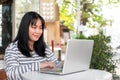 A smiling and positive Asian woman is working remotely outdoors in a city park, using her laptop Royalty Free Stock Photo