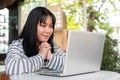 A smiling and positive Asian woman is working remotely outdoors in a city park, using her laptop Royalty Free Stock Photo