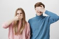 Smiling positive caucasian couple standing close to each other against gray wall. Blonde girl hiding mouth behind palm Royalty Free Stock Photo