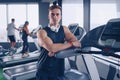 Smiling positive confident male personal instructor with arms crossed arms near treadmill at gym in fitness gym Royalty Free Stock Photo