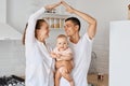 Smiling positive family posing looking at each other with happy facile expression, holding baby daughter in hands, mother and