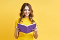 Smiling positive girl reading book on yellow background Royalty Free Stock Photo