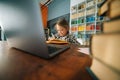 Smiling positive primary child school girl doing homework writing notes in paper notebook sitting at table with laptop. Royalty Free Stock Photo