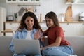 Smiling positive woman nanny and school age girl making video call in laptop sits on couch at home