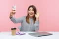 Smiling positive woman in striped shirt saying hello and waving hand looking at smartphone camera, keeping online video call, Royalty Free Stock Photo