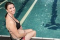 Smiling pregant woman sitting on the edge of the pool