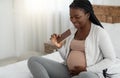 Smiling pregnant african american woman eating bar of chocolate at home Royalty Free Stock Photo