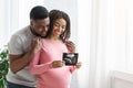 Smiling pregnant black couple showing ultrasound image of their baby