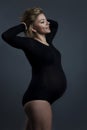 Smiling pregnant woman in black bodysuit. Happy baby waiting. Grey background. Vertical