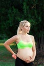 Smiling pregnant woman caress her belly at nature