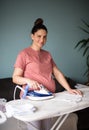 Smiling pregnant woman at home ironing baby laundry