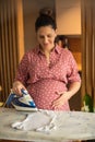 Pregnant woman ironing baby laundry at home Royalty Free Stock Photo