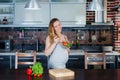 The smiling pregnant woman in kitchen is eating vegetable salad.