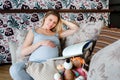 Smiling pregnant woman resting on sofa with child`s toys and reading book. Royalty Free Stock Photo