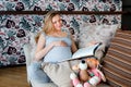 Smiling pregnant woman resting on sofa with child`s toys and reading book. Royalty Free Stock Photo