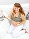 Smiling pregnant woman sitting on sofa with book. Royalty Free Stock Photo