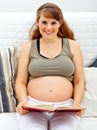 Smiling pregnant woman sitting on sofa with book Royalty Free Stock Photo