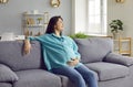 Smiling pregnant woman sitting on sofa at home holding her belly and looking at the window. Royalty Free Stock Photo