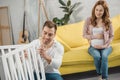 smiling pregnant woman sitting on sofa and looking at happy husband fixing Royalty Free Stock Photo